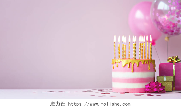 粉红气球和插有蜡烛的生日蛋糕粉红色的生日蛋糕，上面有金色的蜡烛和气球